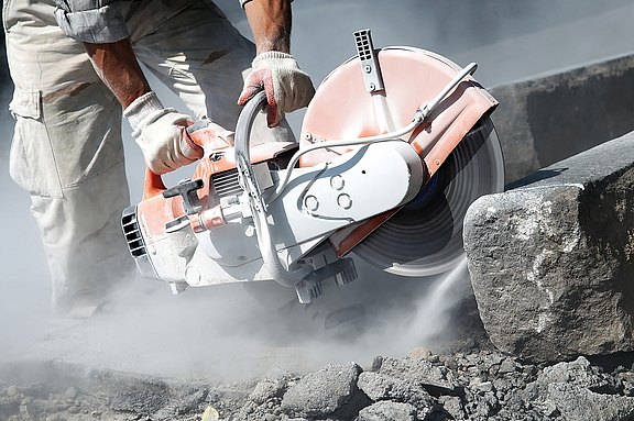 Abbildung eines Baggers beim Abriss eines Gebäudes mit viel Staubentwicklung