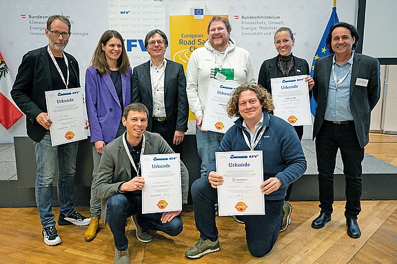 Gruppenbild mit sechs stehenden und zwei knieenden Personen mit fünf Urkunden in der Hand