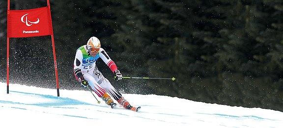 Skirennläufer im Rennanzug und Helm mit Brille und einem angestrengten Gesichtsausdruck bei einem Abfahrtslauf in eine Kurve fahrend.